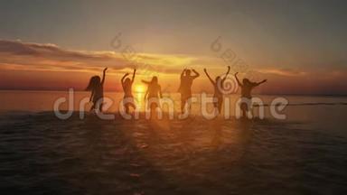 在日落时分，<strong>一群</strong>快乐的朋友在水中<strong>奔跑</strong>-活跃的人们在海滩上度假的剪影